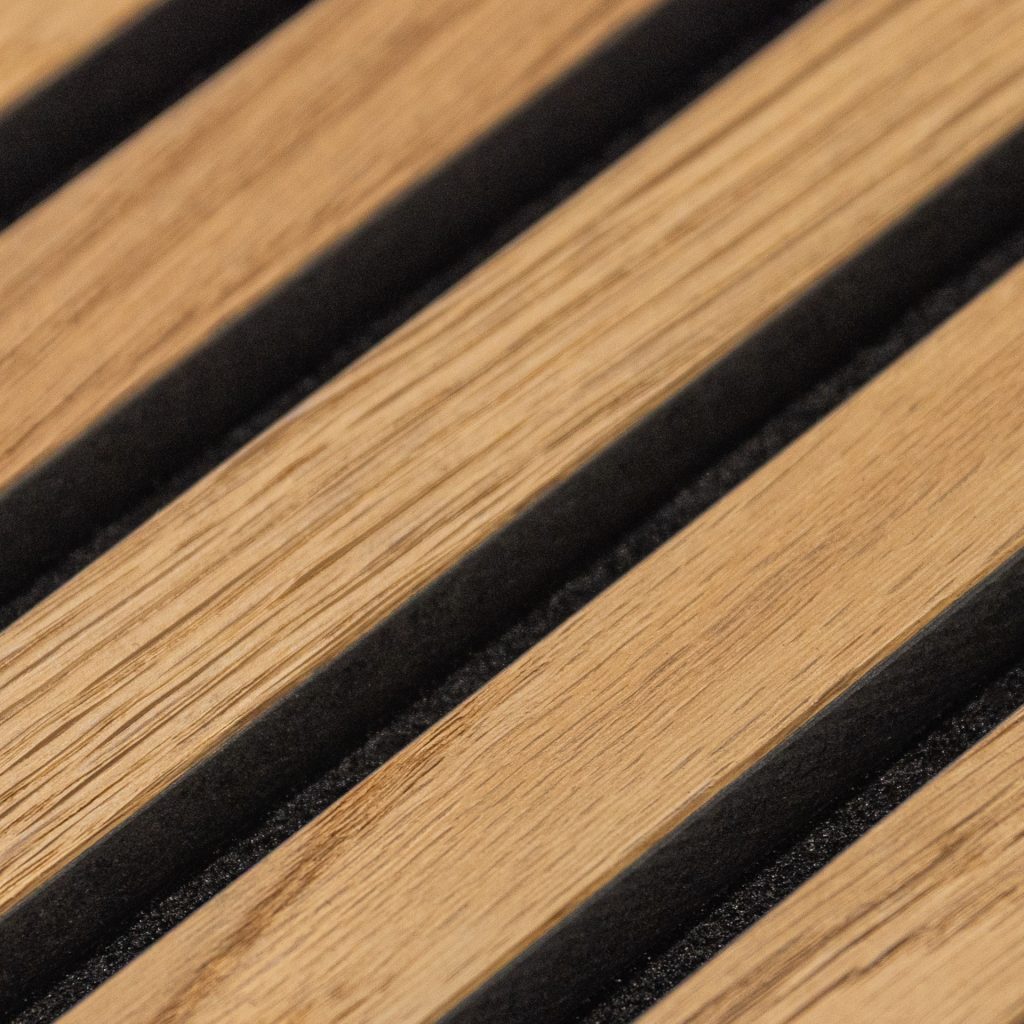 Detalle de panel WoodUpp formado por lamas paralelas de madera clara alternadas con ranuras negras acolchadas. Se aprecian la veta natural y el acabado lijado de las tablas y el contraste textural del relleno oscuro, mostrando el diseño modular y sostenible de productos WoodUpp.