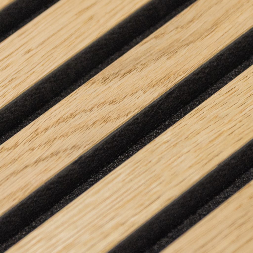 Primer plano de un panel de lamas WoodUpp: listones de madera clara (roble) con ranuras negras rellenas de fieltro acústico, mostrando veta natural y separación regular entre lamas, acabado liso y diseño modular pensado para revestimiento decorativo y acústico de paredes.