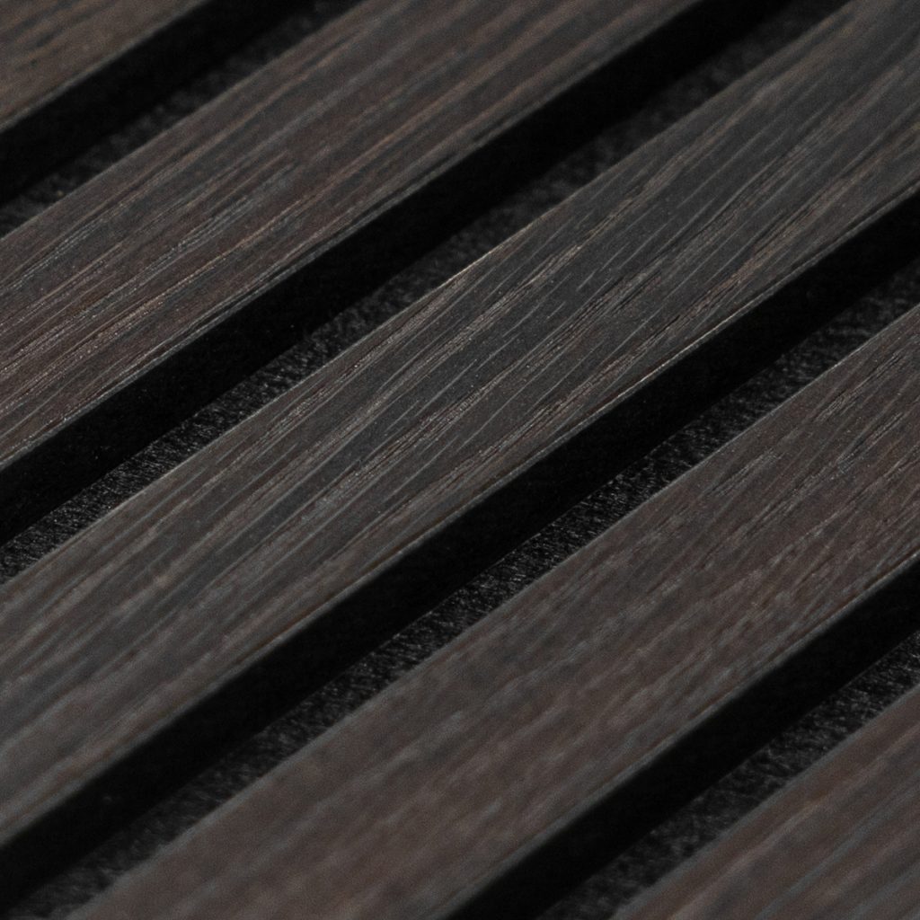 Detalle en primer plano de listones de madera oscura de WoodUpp: lamas inclinadas con veta visible y acabado mate, separadas por ranuras que muestran un respaldo negro texturizado, formando un panel acústico decorativo típico de los productos WoodUpp para revestimiento y control sonoro.