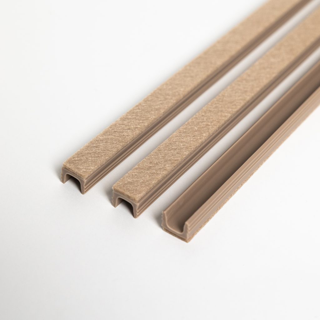 Imagen de WoodUpp que muestra tres perfiles en U de plástico color beige: dos con tira superior de fieltro adhesivo marrón claro y uno abierto sin fieltro, todos con ranura interior para encaje. Dispuestos en diagonal sobre fondo blanco, muestran textura y diseño para protección de madera.