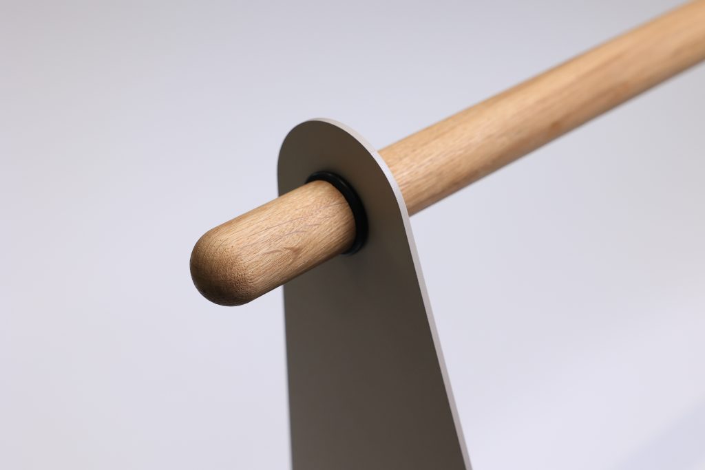 Imagen de WoodUpp: barra cilíndrica de madera clara (roble) con extremo redondeado, encajada en un soporte metálico minimalista gris con abertura circular y anillo negro que la sujeta. Diseño limpio y detalles visibles de la veta de la madera y acabado natural.