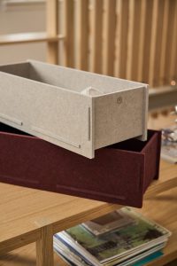Caja organizadora modular de WoodUpp: dos bandejas rectangulares de fieltro, una beige y otra granate, con encajes laterales y acabado liso, apiladas sobre una mesa de madera. Diseñadas para almacenar objetos y textiles, muestran el logotipo circular de WoodUpp en el panel frontal.