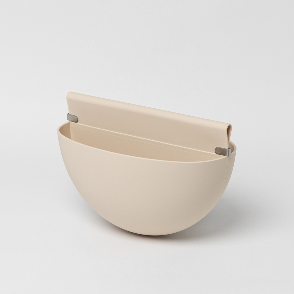 Primer plano del bolsillo de almacenamiento colgante de color beige de WoodUpp. Este accesorio tiene una forma semicircular elegante y una solapa superior con clips metálicos, diseñado para integrarse en los paneles de listones de madera, sobre un fondo blanco liso.